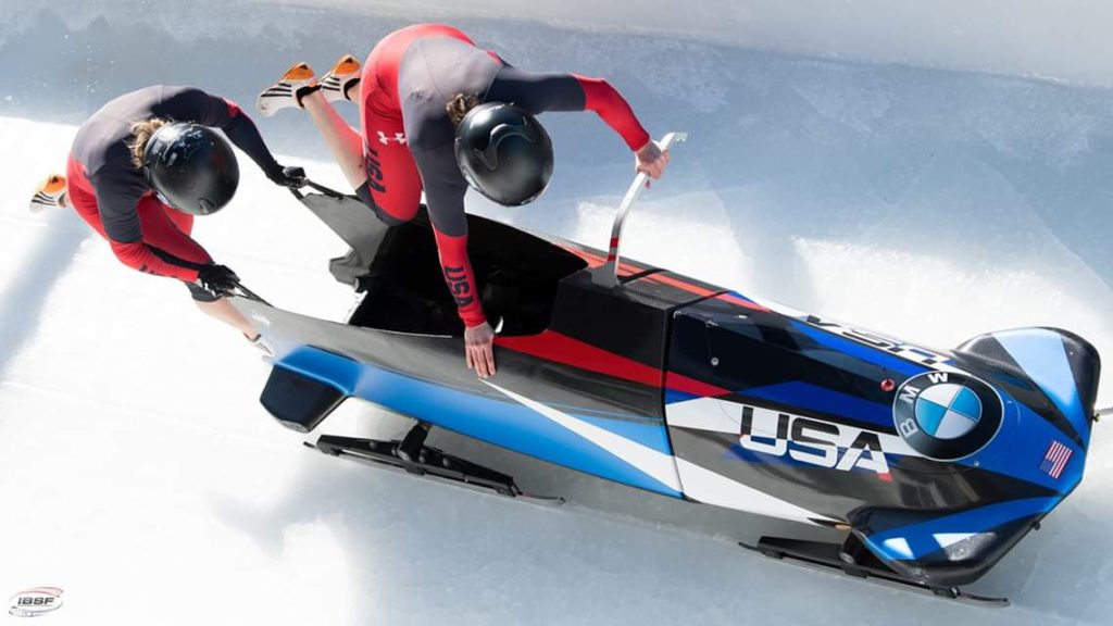 2 girls trying new things by running on ice and jumping into a bobsled at the start of a race